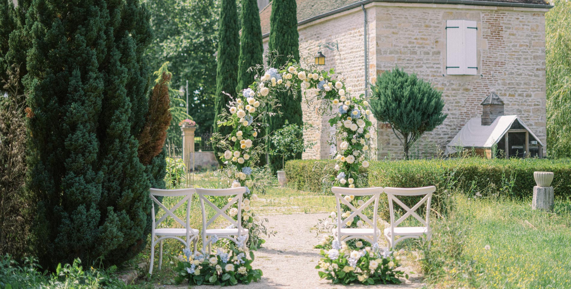 Arche de mariage élégante avec roses crèmes au milieu d'un jardin français